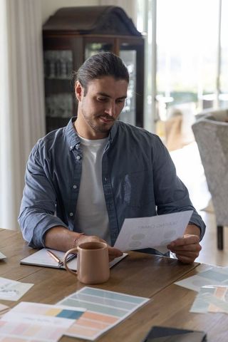 Man reviewing color swatches and printed charts at wooden table home workspace
