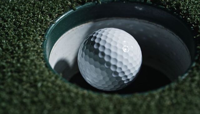 Close-up golf ball nesting in cup on lush putting green showing precision putting moment