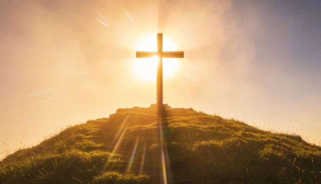 Sunlit wooden cross on grassy hilltop radiant halo and lens flare at golden hour