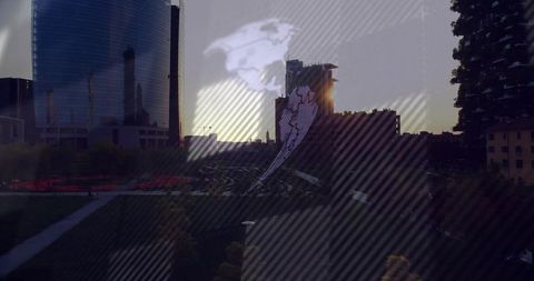 Mirrored glass tower reflecting sunset with globe overlay over urban park skyline