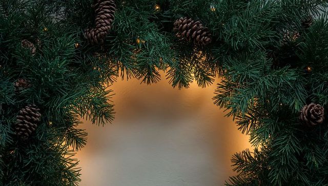 Evergreen garland framing warm amber lights on cream wall with pine cones and bokeh glow