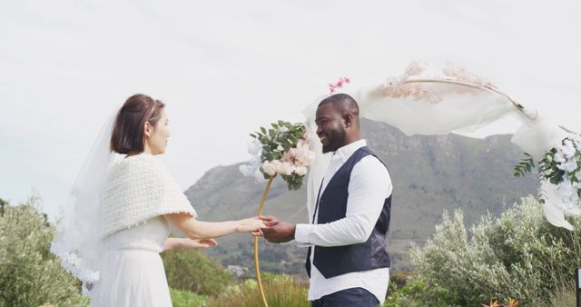 Image of happy diverse bride and groom holding hands, smiling and dancing at outdoor wedding. Marriage, love, happiness and inclusivity concept.