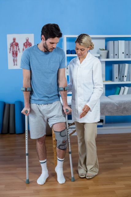 Physiotherapist helping patient to walk with crutches in clinic