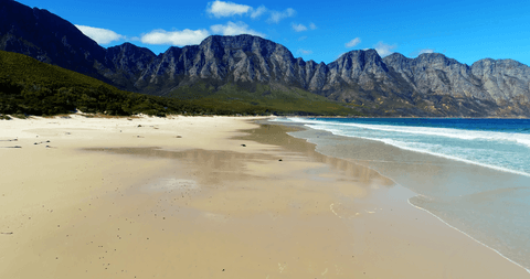 Transparent sandy beach with mountainous background and blue sky