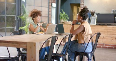 Two women brainstorming over laptops in bright café coworking space