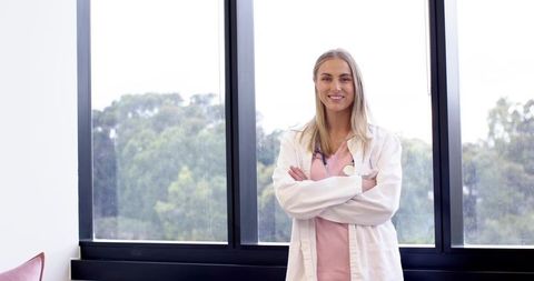 Confident clinician standing with arms crossed by large window in bright modern clinic
