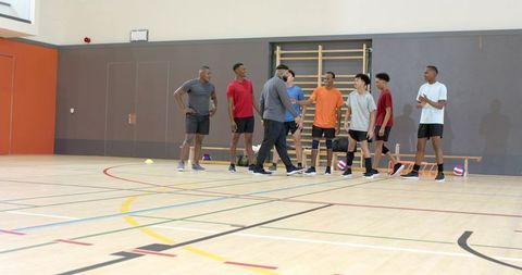 Diverse male volleyball team warming up and receiving coaching on indoor gym court