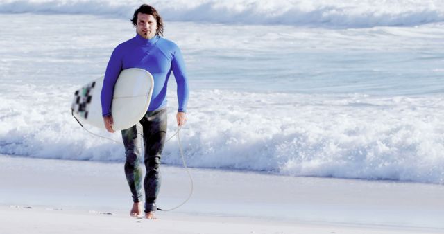 A Caucasian middle-aged man walks on the beach holding a surfboard, with copy space. He appears ready for a surfing session, with the ocean waves in the background suggesting an active lifestyle.