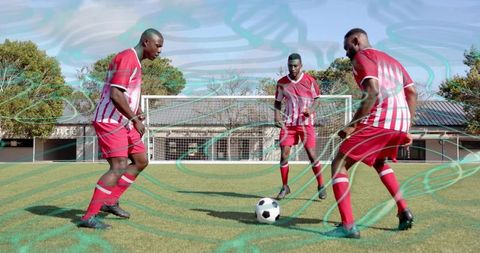 Three soccer players training on sunny grass field wearing red and white uniforms