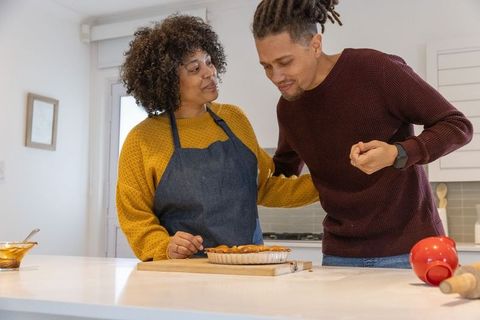 Couple sharing homemade pie at kitchen island, woman in apron steadying partner