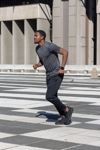 African American Man Running in Urban Plaza Wearing Smartwatch and Athletic Sportswear