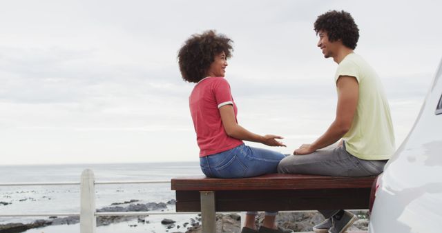 African american couple smiling while talking to each other sitting on a bench on the promenade. love and relationship concept