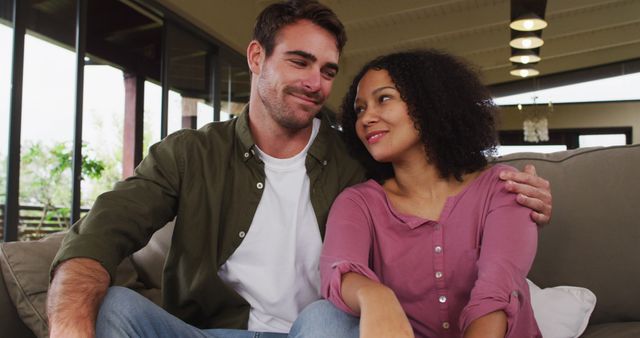 Biracial couple smiling while looking at each other sitting on the couch at vacation home - Download Free Stock Photos Pikwizard.com