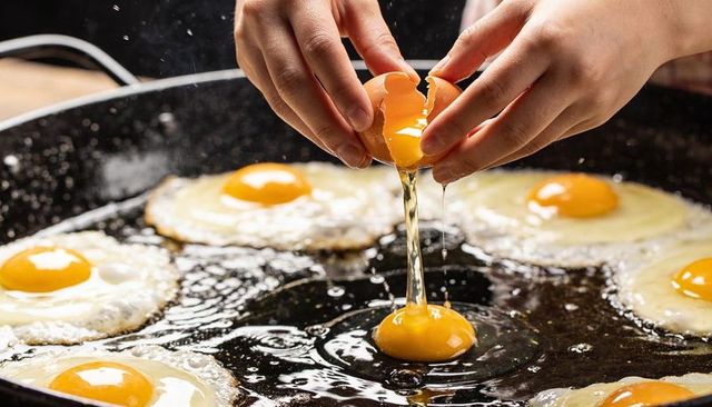 Hands cracking fresh eggs over hot skillet, sunny-side-up eggs frying and oil sizzling