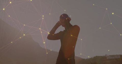 Standing man connecting to digital network at sunset silhouette over mountain horizon