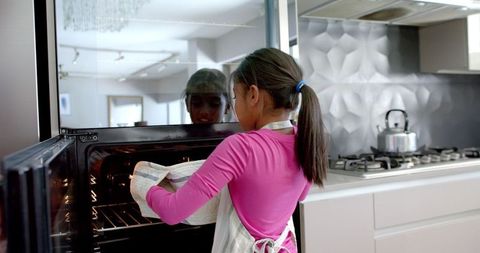Young girl baking cakes from oven in modern kitchen