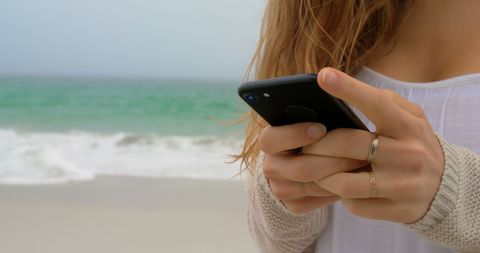 Woman Texting on Beach with Ocean Waves in Background