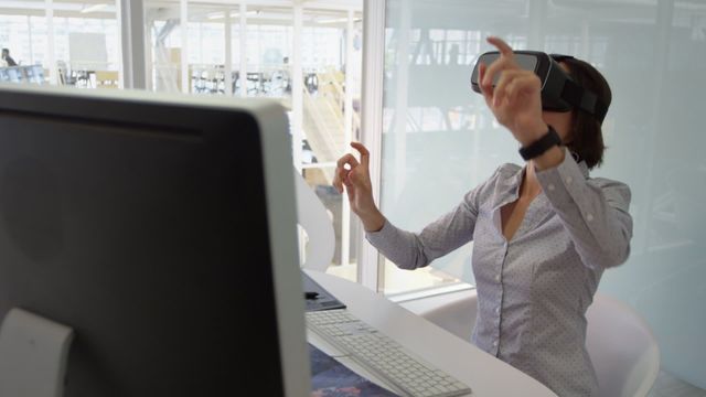 Businesswoman interacts with virtual reality headset in an office environment, conveying concepts of technology use at work, innovation, and future-focused business practices. Useful for articles or advertisements relating to virtual reality technology, digital workspaces, or modern office culture representation.