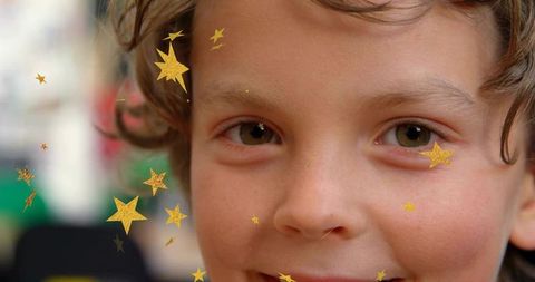 Smiling curly-haired child wearing gold star stickers, sparkling bokeh, joyful closeup portrait