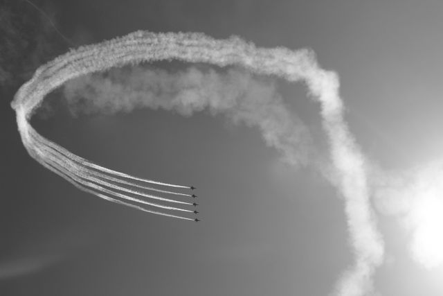 Black and white image showcasing six jets flying in formation with detailed smoke trails against clear sky. Ideal for use in articles about airshows, aviation technology, and team dynamics. Can also be used in promotional materials for airshows and aviation events.