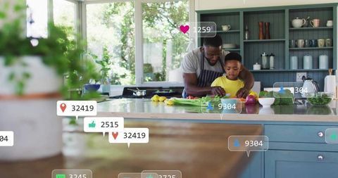 Father guiding son chopping healthy vegetables on kitchen island with social media overlays