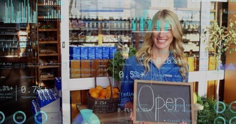 Smiling owner holding open chalkboard at vibrant produce shop wearing denim shirt with oranges