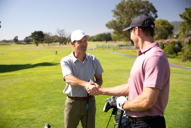 Two Caucasian male golfers practicing on a golf course on a sunny day wearing caps and golf clothes, shaking hands holding golf clubs. Hobby healthy lifestyle leisure.