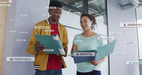 Coworkers reviewing documents with digital data overlays, holding binders by glass partition