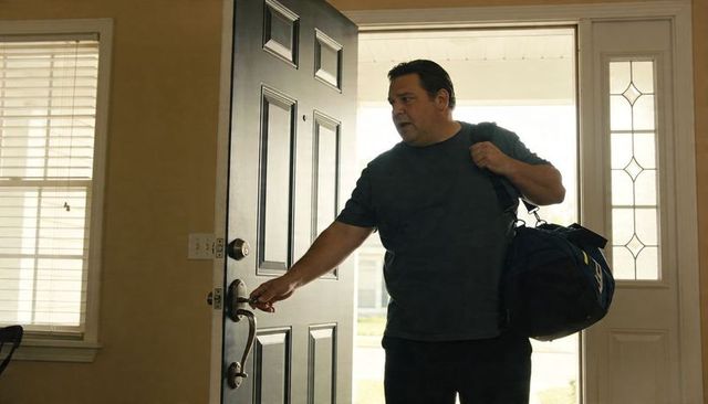 Man entering home carrying duffel bag reaching for door handle in sunlit foyer