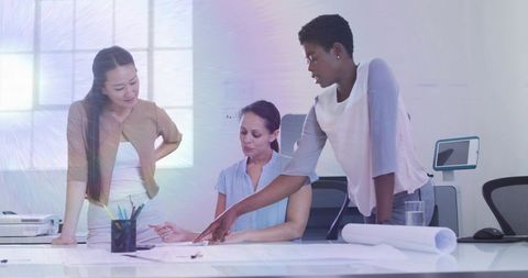 Three women collaborating over blueprint plans and documents in bright modern workspace
