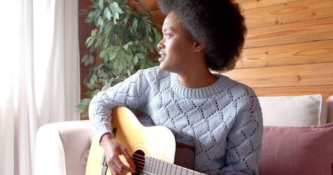 Woman with afro playing guitar at home