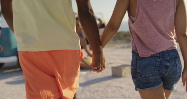 Group of happy diverse friends with campervan holding hands and walking at beach. Summer, vacation, friendship and travel.