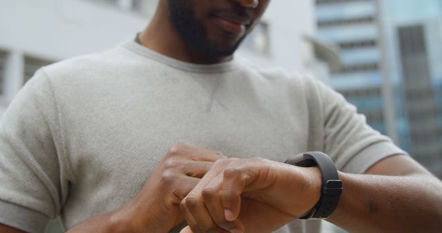 Casual setting shows a man checking his fitness tracker or smartwatch for daily activity and steps in an urban area. Useful for topics on fitness, technology in health, modern lifestyles, and tracking activity. Ideal for health-related articles, tech products advertisement, urban living, and lifestyle blogs.