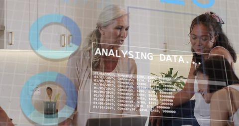 Senior mentor guiding young women collaborating and analyzing data at kitchen counter