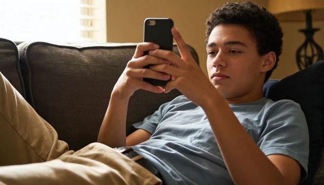 Reclining teen scrolling smartphone on living room couch relaxing at home