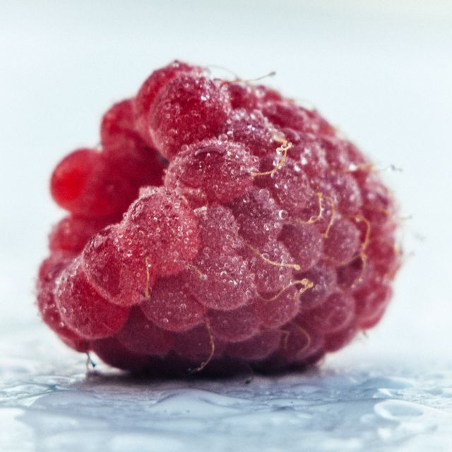 This close-up captures a frozen raspberry covered in tiny ice crystals, highlighting its vibrant red color and detailed texture. Ideal for illustrating topics related to frozen foods, freshness, healthy eating, fruit preservation, or food photography. Useful for websites, blogs, advertisements, and educational materials about cold storage of fruits or promoting nutritious food choices.