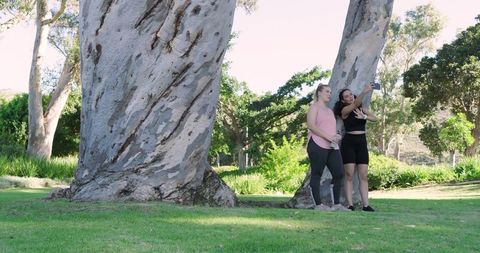 Active young women taking selfie in green park with tall trees