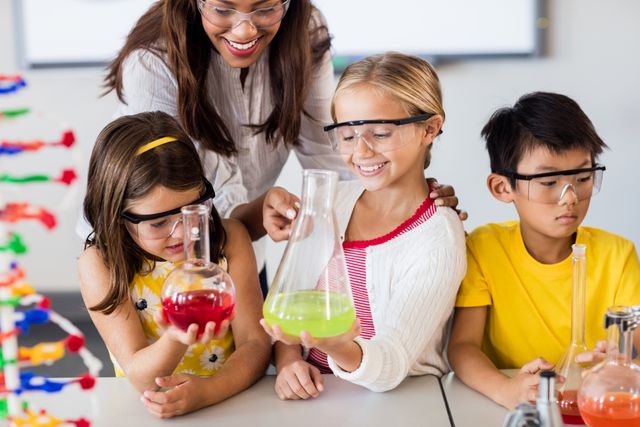 Teacher guiding young students in a science experiment, wearing safety goggles and holding beakers with colorful liquids. Ideal for educational content, school promotions, STEM programs, and science-related articles.