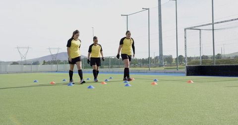 Female Soccer Players Dribbling Through Colorful Cones on Training Field