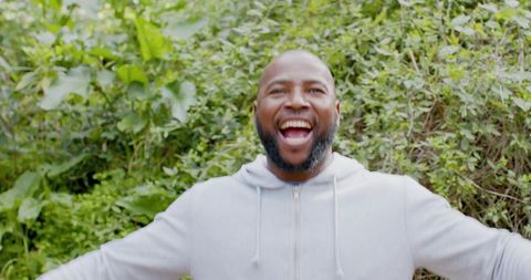 Joyful mature African American man laughing outdoors in gray hoodie among lush greenery
