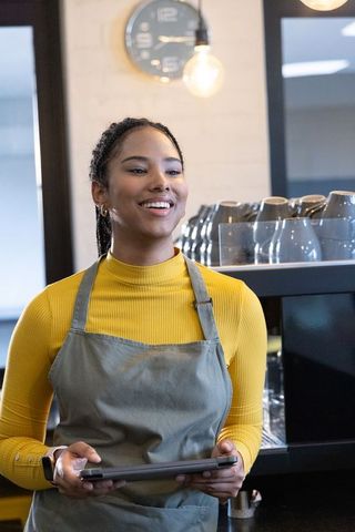 Smiling african american barista using tablet behind modern cafe counter