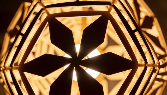 Geometric hexagonal pendant lamp casting warm amber glow through floral cutouts