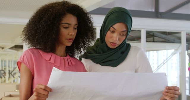 Two professional women analyzing architectural plans at workplace - Download Free Stock Images Pikwizard.com