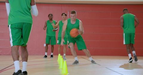 Basketball team practicing dribbling agility drill around cones on indoor court