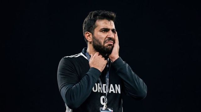 Tense athlete wearing jordan tracksuit pressing cheek and adjusting lanyard under spotlight