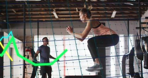 Female athlete performing plyometric box jump in industrial gym with neon data overlay