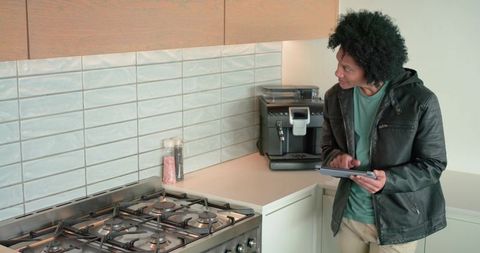 African american man holding tablet in modern kitchen glancing at stove and espresso machine