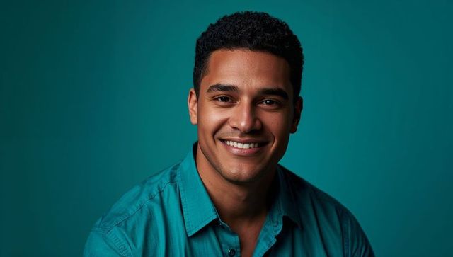 Smiling professional male headshot making eye contact teal shirt modern studio portrait