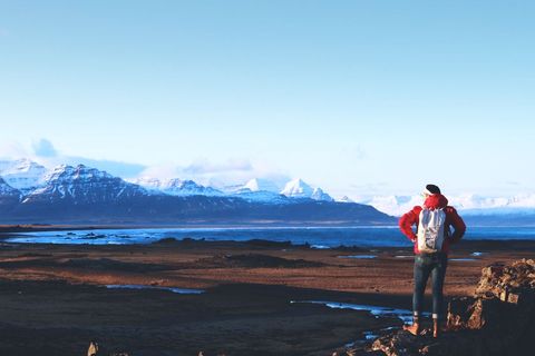Solo hiker overlooking rugged coastline and distant snow-capped mountains at golden hour