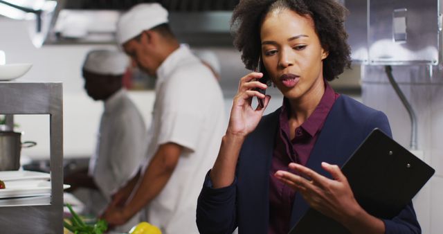 African american female manager talking on smartphone in restaurant kitchen. Working in a busy restaurant kitchen.